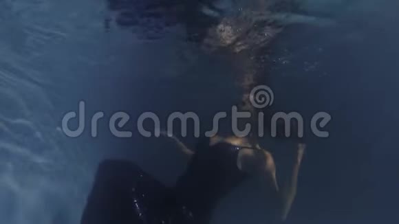 穿着蓝色闪闪发光连衣裙的女人正在水下游泳靠近水面4K视频的预览图