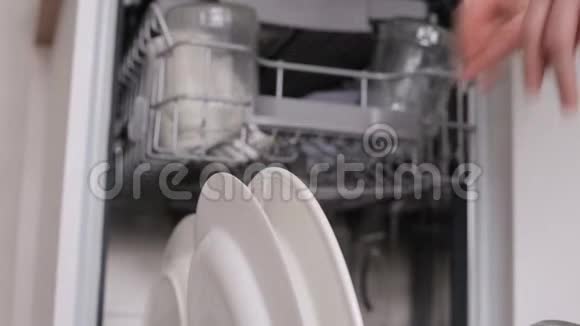 女人把白色脏盘子放进洗碗机篮子和特写手视频的预览图