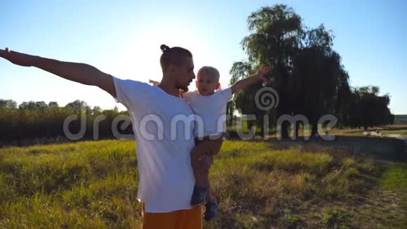 英俊的父亲和小儿子在草地上举着手做飞机的肖像小爸爸抱着儿子视频的预览图