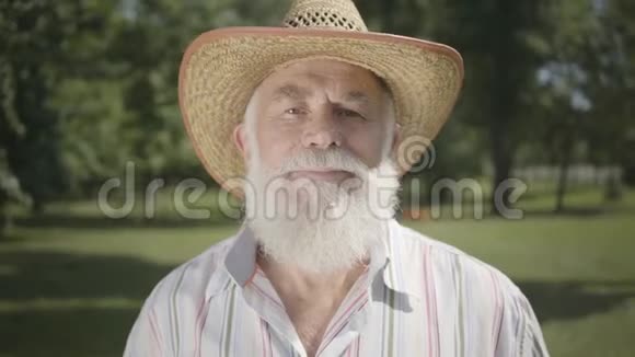 画像上的白发老人戴着草帽微笑着站在公园里看着摄像机户外休闲视频的预览图