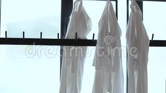 几个白色浴袍挂在衣架上靠近一扇窗户可以看到一个热气腾腾的贝森视频的预览图
