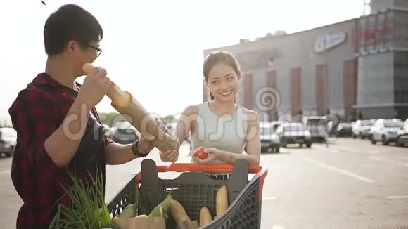 嘲笑美丽的亚洲夫妇他们手里拿着装满不同用品的购物车站在大超市附近视频的预览图