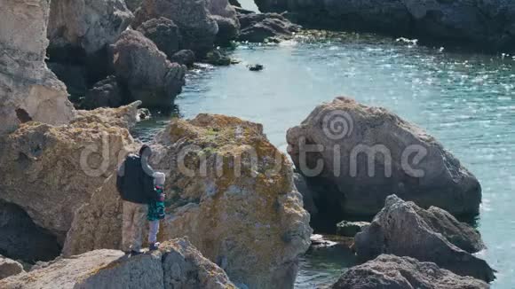 父亲和孩子在一块大石头上看着大海视频的预览图