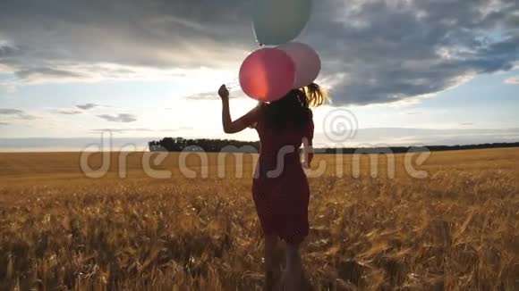 在日落时分穿着红色衣服的快乐女孩手里拿着气球跑过金色年轻女子视频的预览图