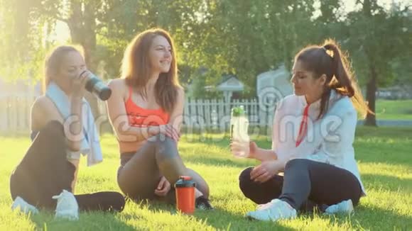三个女朋友在慢跑后坐在草地上喝着金属瓶和塑料瓶的水视频的预览图