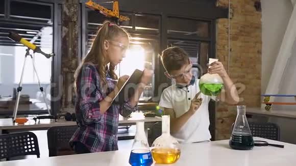 两名戴着安全护目镜的白种人小学生在烧瓶和干冰中试验绿色液体视频的预览图