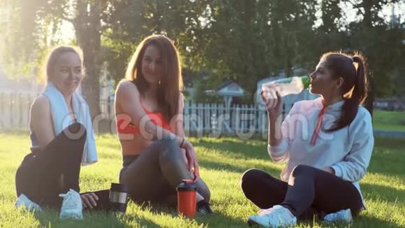 三个女朋友跑完后正坐在草地上她们在聊天喝着瓶子里的水视频的预览图