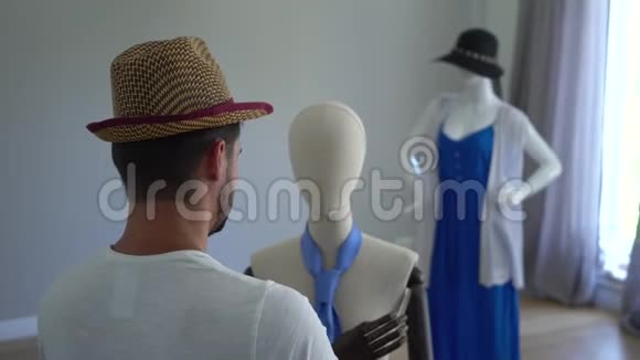 一个年轻人把帽子戴在人体模型的头上在缝纫室或视频的预览图