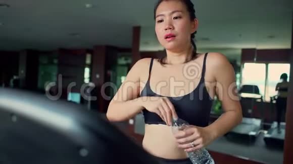 年轻多汗疲惫的亚洲跑步女子慢跑后在健身房跑步机上放松行走和呼吸视频的预览图