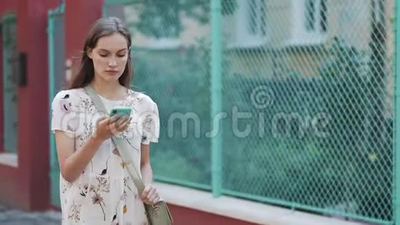 穿着白色花裙带袋的漂亮女人用她的智能手机语音指挥做语音视频的预览图