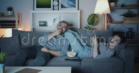 美丽的一对夫妇在公寓沙发上看电视晚上放松笑着视频的预览图