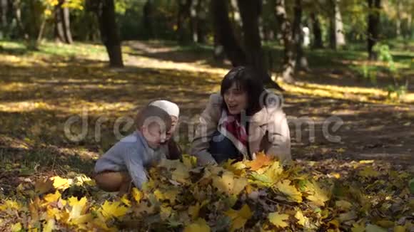 快乐的妈妈和孩子们在公园里扔树叶视频的预览图