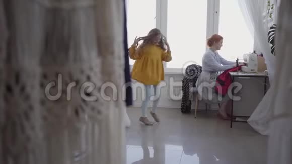 红发女人在灯光室的窗户附近的桌子旁缝衣服小女儿在旋转视频的预览图