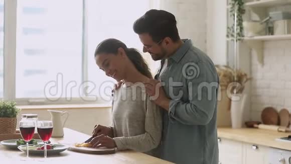 年轻快乐的丈夫拥抱妻子切菜色拉厨房视频的预览图