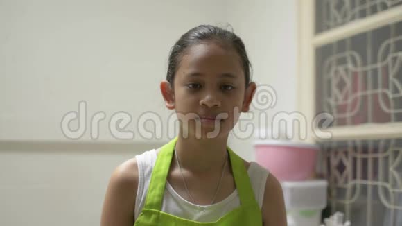 肖像滑稽可爱的女孩穿着围裙微笑一边拿着食物载体和铲子在厨房视频的预览图