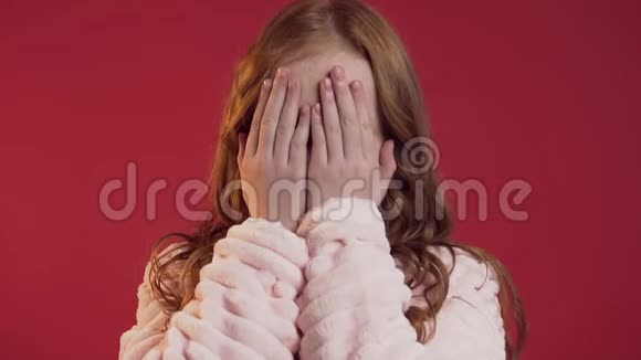 美丽的肖像可爱的快乐少女红色长发覆盖她的脸手掌在红墙的背景上视频的预览图