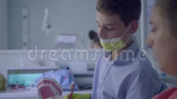 牙医办公室的十几岁男孩医生教病人用模拟下颌刷牙口腔科视频的预览图