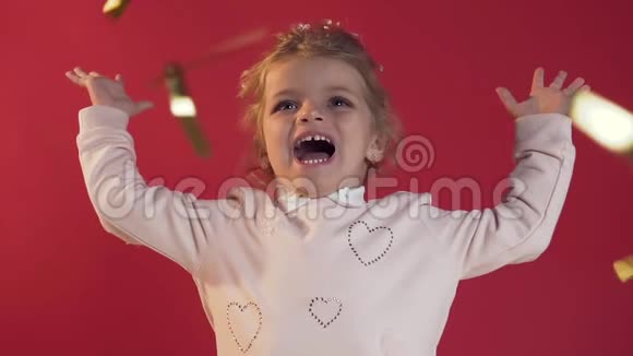 亲密的可爱活泼的小女孩带着迷人的微笑在工作室的红色背景上玩着五彩纸屑视频的预览图