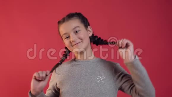 可爱的微笑少女与两个辫子摆在相机上的红墙背景视频的预览图