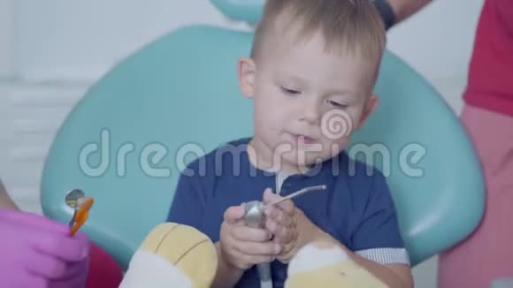 坐在牙科办公室椅子上的无忧无虑的小男孩可爱的孩子玩毛绒玩具牙科治疗医疗视频的预览图