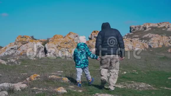 父亲和女儿穿着暖和的衣服走在岩石中间视频的预览图