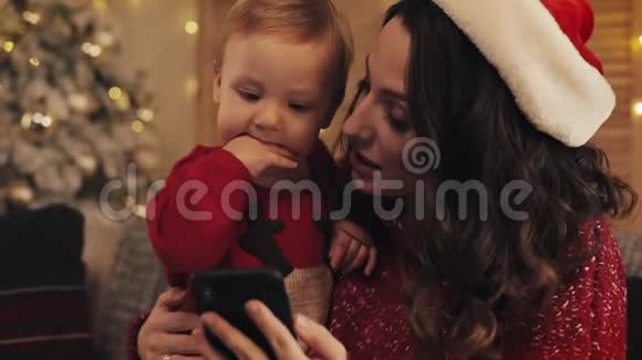 小美女妈妈戴着圣诞帽坐在沙发上可爱的小男孩面带微笑视频的预览图