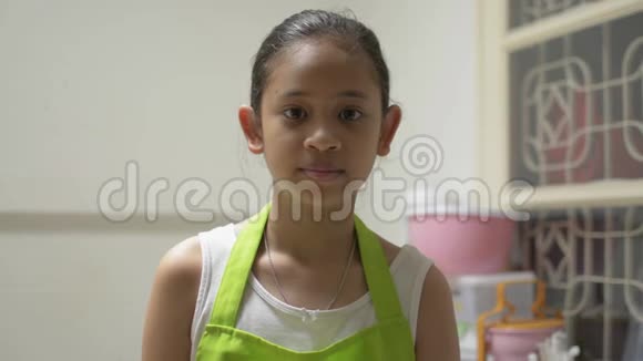 肖像滑稽可爱的女孩穿着围裙微笑一边拿着勺子和铲子在厨房视频的预览图