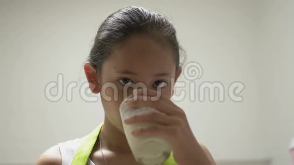 肖像健康可爱的女孩穿着围裙喝着一杯牛奶在家里高兴地用舌头舔着嘴视频的预览图