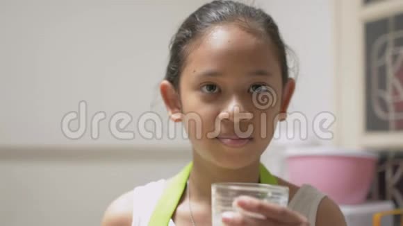 肖像健康可爱的女孩穿着围裙喝着一杯牛奶在家里高兴地用舌头舔着嘴视频的预览图