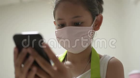 亚洲可爱的女孩穿着围裙戴着防护面具用手机与她的朋友进行社交在线交流视频的预览图