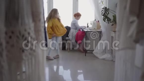 美丽的红发女人缝衣服坐在桌子旁边的窗户在灯光室小女儿在跳舞视频的预览图
