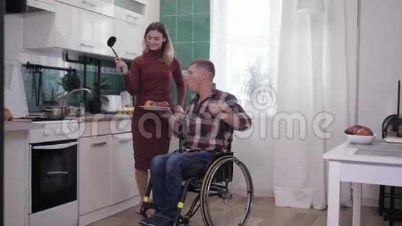 家庭舞蹈坐轮椅的男人和妻子在厨房做饭时享受快乐的消遣视频的预览图