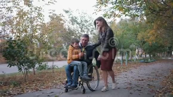 一个坐轮椅的残疾人和他的女朋友一起走在秋天的大街上骑着一个男孩在摇篮上视频的预览图