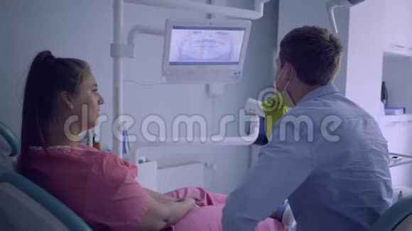 戴着医疗面具的年轻人在屏幕上向他的女病人展示她上下颚的照片那个女人视频的预览图