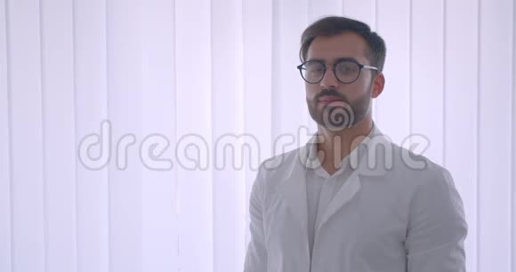 一幅成年白种人英俊的男医生戴着眼镜看着镜头在白色的房间里开心地笑着视频的预览图