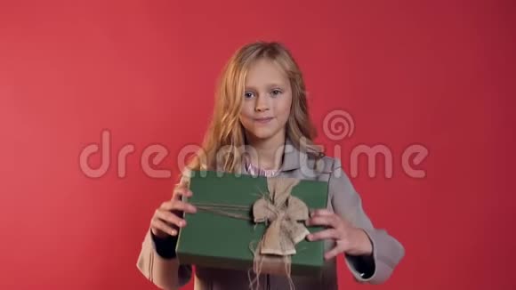 可爱的金发少女模特长发在相机上展示包装良好的盒子背景是红墙视频的预览图