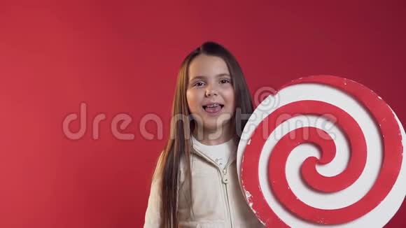 用露出舌头的牙套手里拿着塑料棒棒糖在红色的背景上把笑眯眯的少女合上视频的预览图