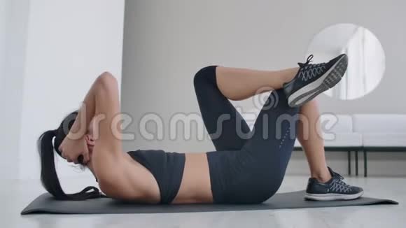 白人黑发女人躺在地毯上做腹肌锻炼每天在家锻炼身体保持健康视频的预览图