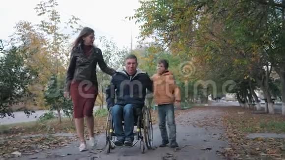 家庭关系快乐的父亲残疾人坐在轮椅上和他快乐的家人沿着秋街散步视频的预览图