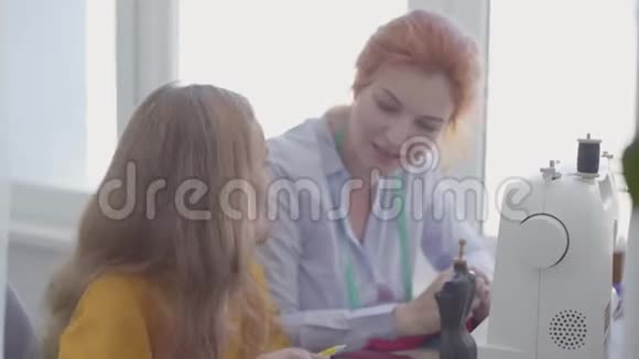 小女孩正坐在前台的桌子旁红发的妈妈在旁边缝衣服视频的预览图
