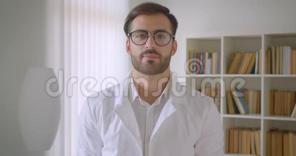 在图书馆里戴着眼镜的成年白种人英俊的男医生看着镜头开心地笑着的特写照片视频的预览图