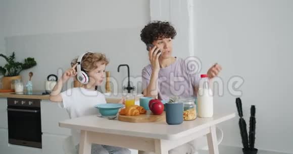 女孩在厨房打电话儿子在耳机里听音乐视频的预览图