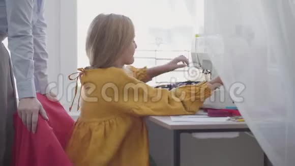 小女孩学着如何缝制坐在靠窗的桌子旁的衣服而她的红头发的母亲在帮助和帮助视频的预览图