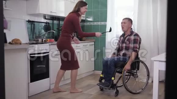 坐在轮椅上的快乐残疾人正在厨房里和女朋友一起跳舞一边做饭视频的预览图