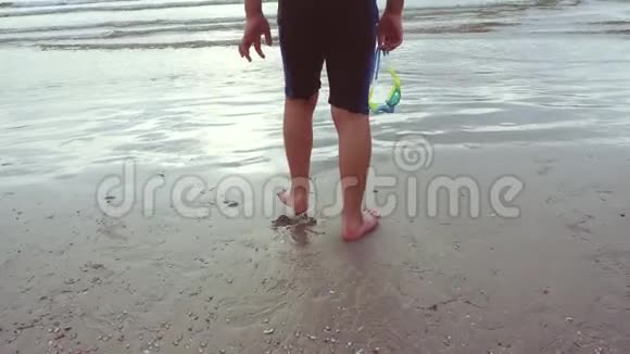 一个穿泳衣的男孩正从海滩走向大海视频的预览图