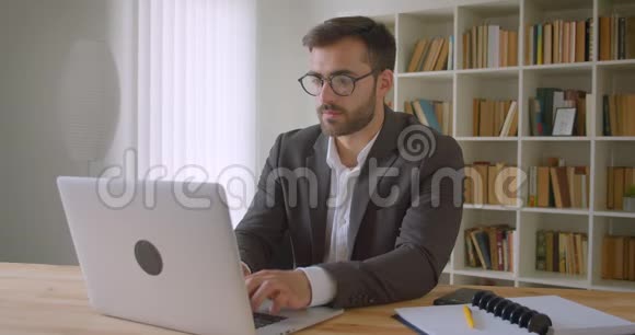 戴眼镜的白种人成年英俊商人的特写肖像他用笔记本电脑在办公室里体贴入微视频的预览图