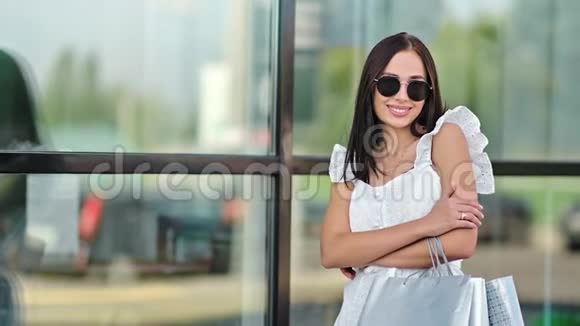 时尚微笑的年轻女士戴着时髦的太阳镜在橱窗里摆着购物袋视频的预览图