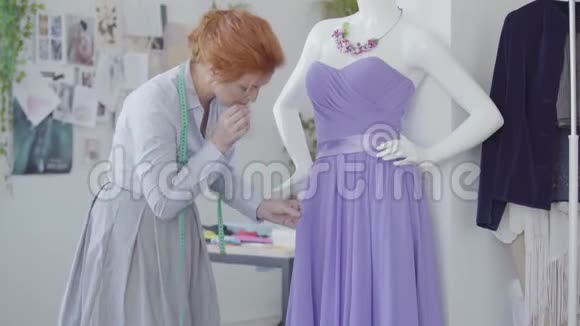 一位漂亮的红发女人正在为一件漂亮的紫色连衣裙做剪裁她挂在人体模型上视频的预览图