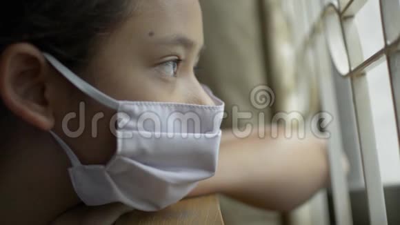 亚洲可爱的女孩戴着防护面具绝望地看着窗外的COVID19疫情视频的预览图