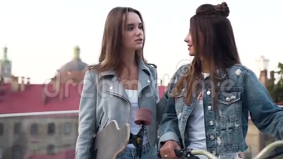 可爱的快乐的年轻女人长发穿着时髦的夹克拿着自行车在观景台上交谈视频的预览图